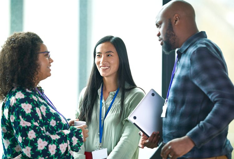 Three individuals wearing conference lanyards have a stand up discussion.