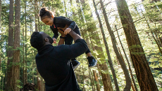 Un homme qui tient une petite fille dans les airs dans une forêt